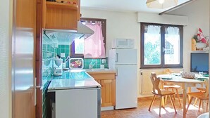 A compact kitchen with wooden cabinets, a refrigerator, a microwave, and a dining area with a table and chairs. - Sunny 2BR Mezzanine Apt with Mountain Views, Fireplace, Near Shops & Lifts, Sleeps 6 (Le Grand-Bornand)