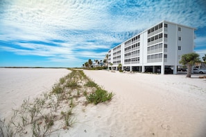 A beachfront hotel with multiple balconies, a sandy beach in the foreground, and a clear sky. - Come Stay at Beautiful Gulf Front Castle Beach Condo 302 on Fort Myers Beach! (Fort Myers Beach)