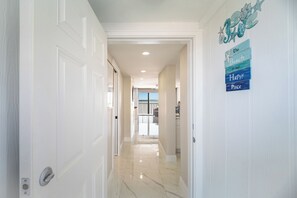 A hallway with a view to a balcony, a sign with a beach theme, and a door with a silver handle. - Come Stay at Beautiful Gulf Front Castle Beach Condo 302 on Fort Myers Beach! (Fort Myers Beach)
