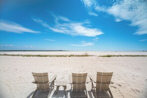 Ein Strand mit drei Stühlen, die auf den Ozean ausgerichtet sind, bewölkter Himmel und ferner Horizont.