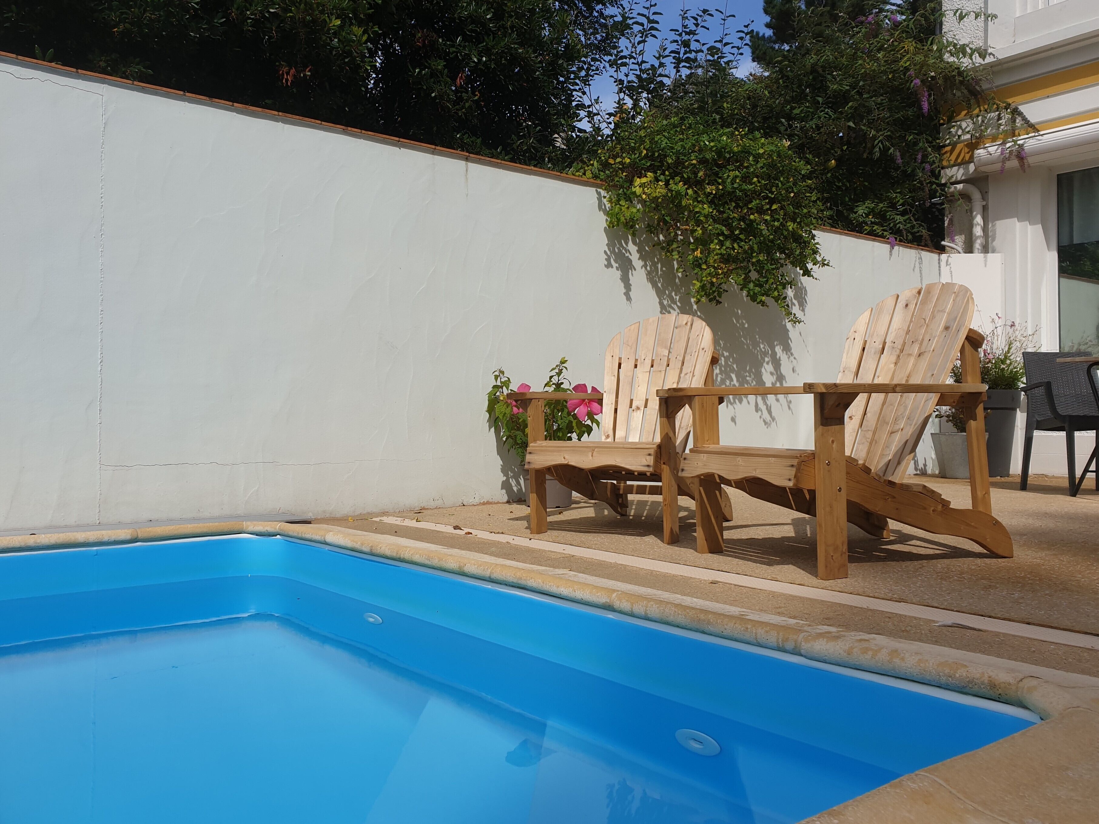 A swimming pool with two wooden Adirondack chairs and a potted plant nearby.