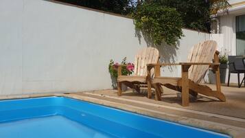 A swimming pool with two wooden Adirondack chairs and a potted plant nearby.