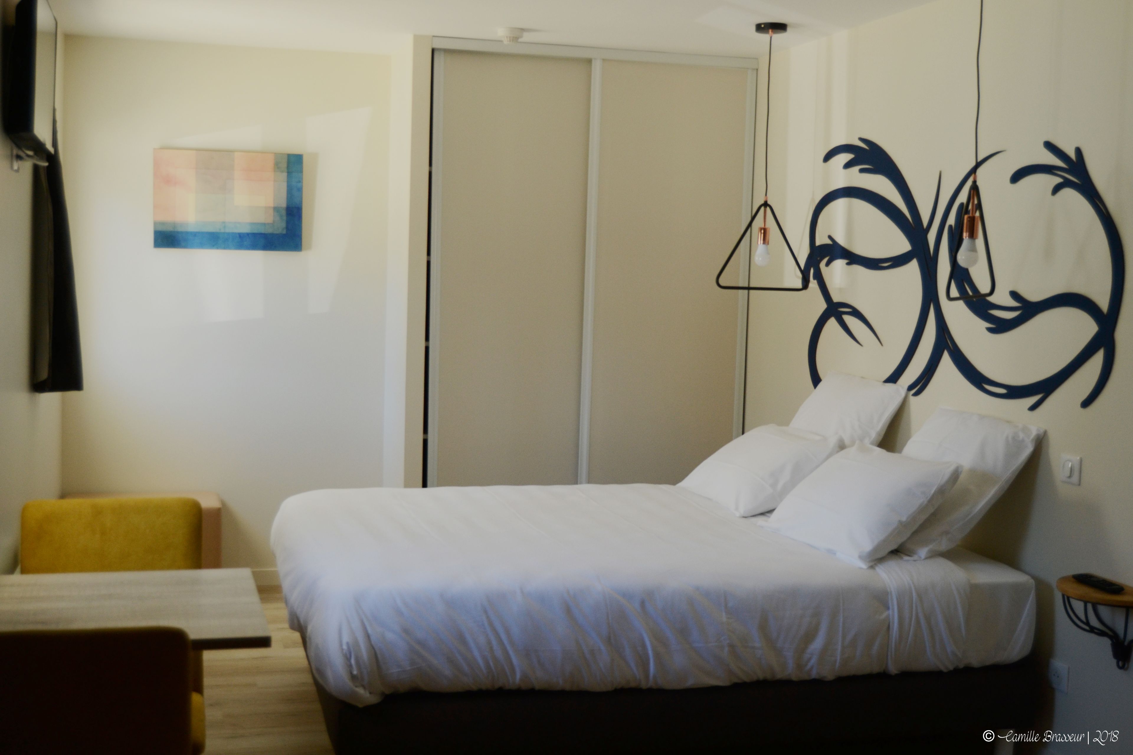 Een slaapkamer met een bed, nachtkastje, stoel, kledingkast en een decoratie aan de muur.