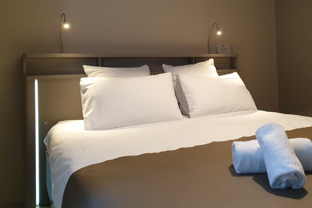 A neatly made bed with white linens and pillows, a wooden headboard, and two bedside lamps.