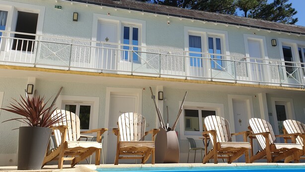 A hotel with a pool area, wooden chairs, and a potted plant. - Le Bercail (Saint-Jean-de-Monts)