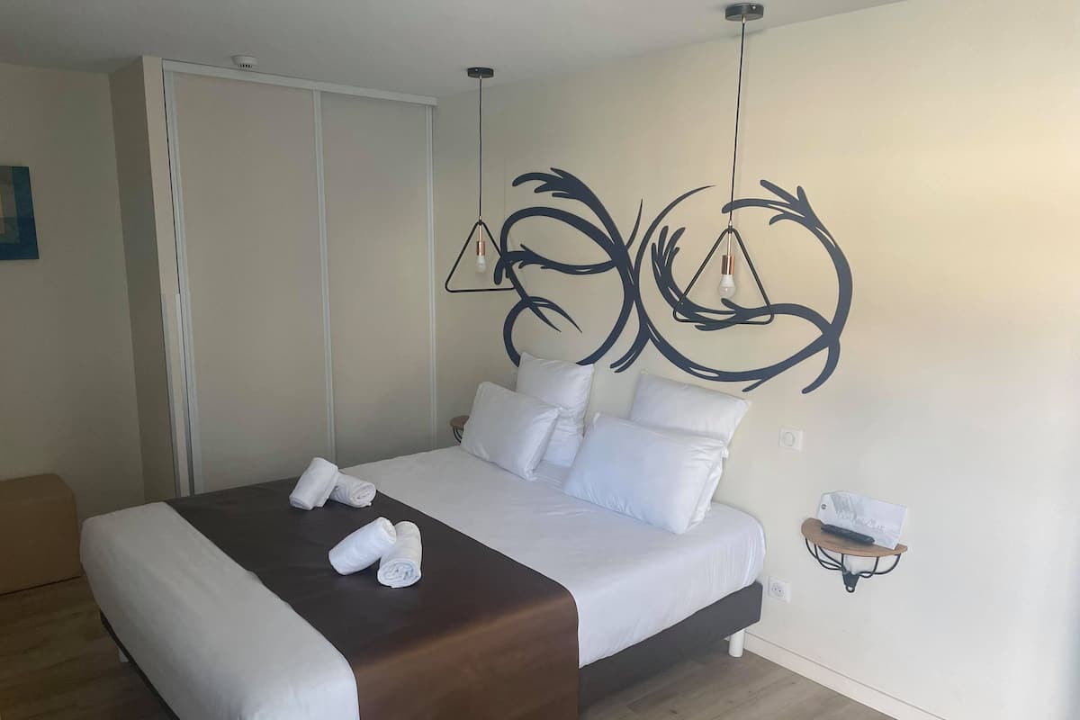 A neatly made bed with white linens and a brown headboard, a wall-mounted light fixture, and a small bedside table with a tissue box.