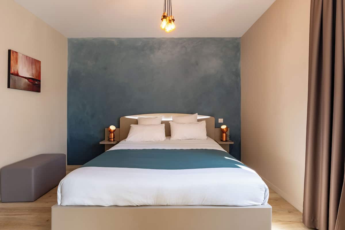 A modern bedroom with a large bed, bedside lamps, a bench, and a painting on the wall.