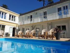 Área de piscina com cadeiras de madeira e piscina.