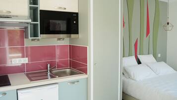 A compact kitchen with a microwave, sink, and dishwasher. Adjacent is a bed with a green and red striped wall.