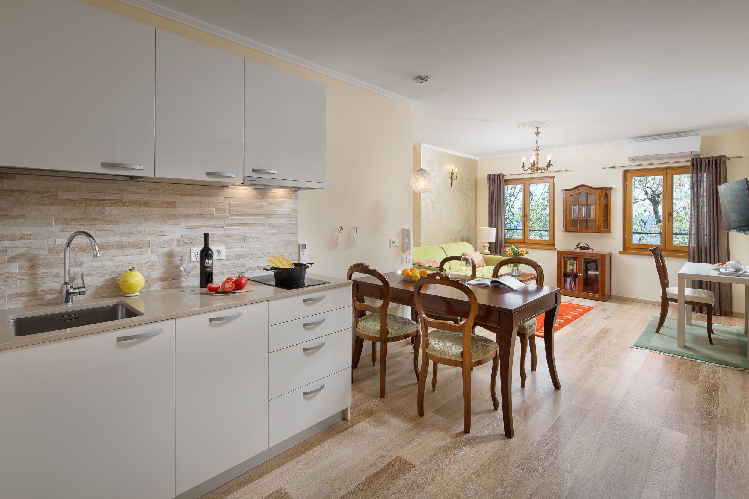 A modern kitchen with white cabinets, a built-in oven, and a dining area with wooden chairs and a table.