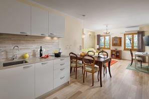 A modern kitchen with white cabinets, a built-in oven, and a dining area with wooden chairs and a table.