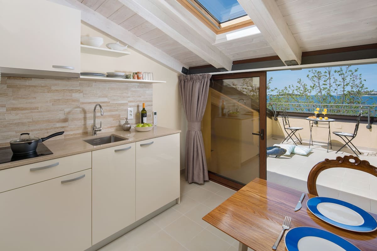 A modern kitchen with a skylight, a dining area with blue plates, and a view of the sea.