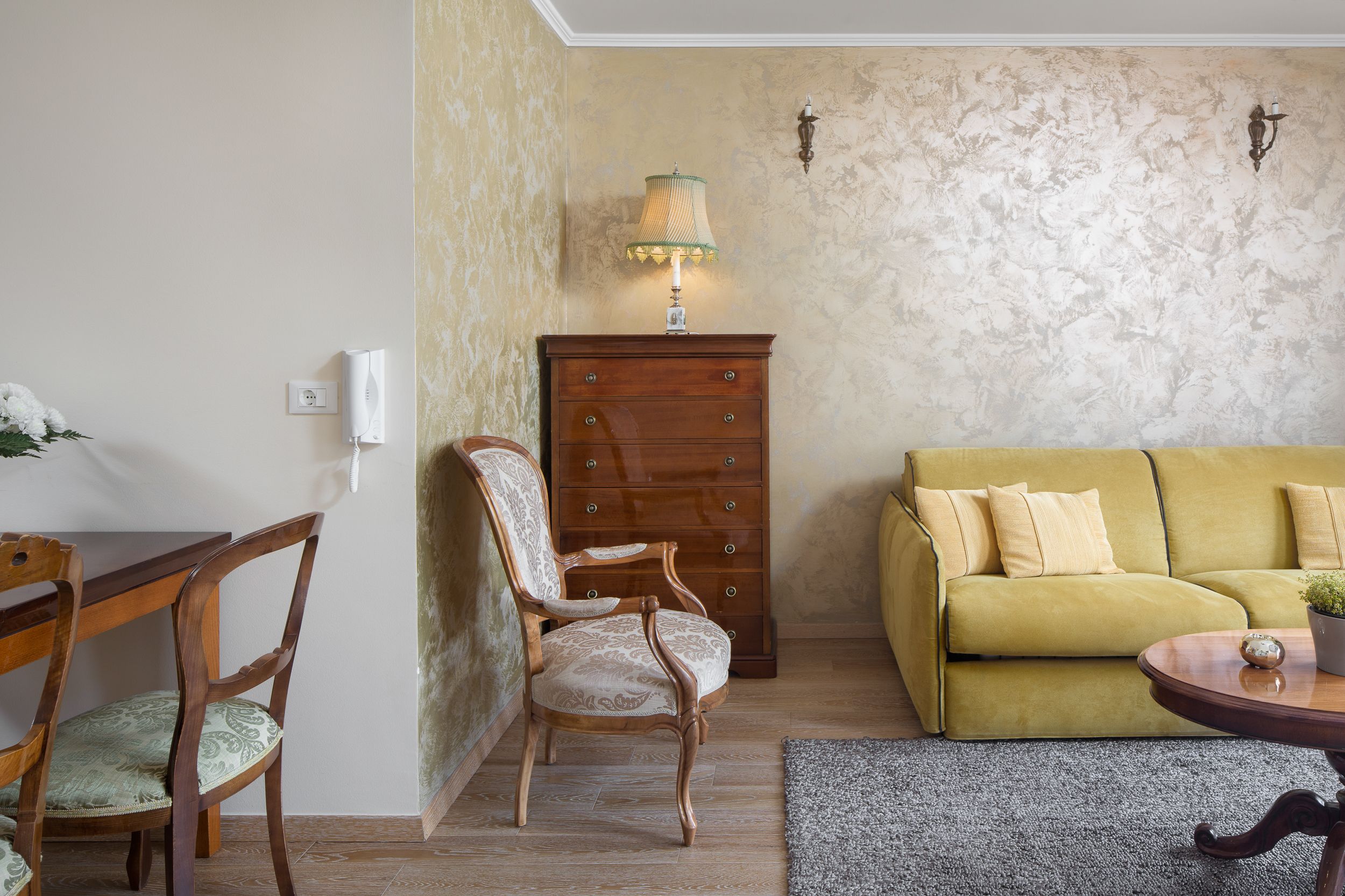 A living room with a wooden chair, a yellow sofa, a wooden table, and a lamp.