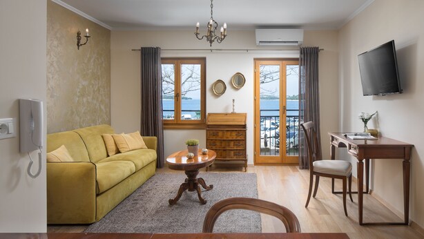 A living room with a sofa, a table, a TV, and a view of the outdoors. - Valdibora Seaview Residence (Rovinj)