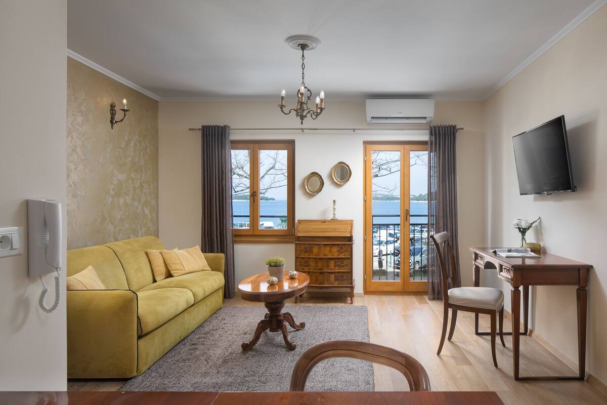 A living room with a sofa, a table, a TV, and a view of the outdoors.