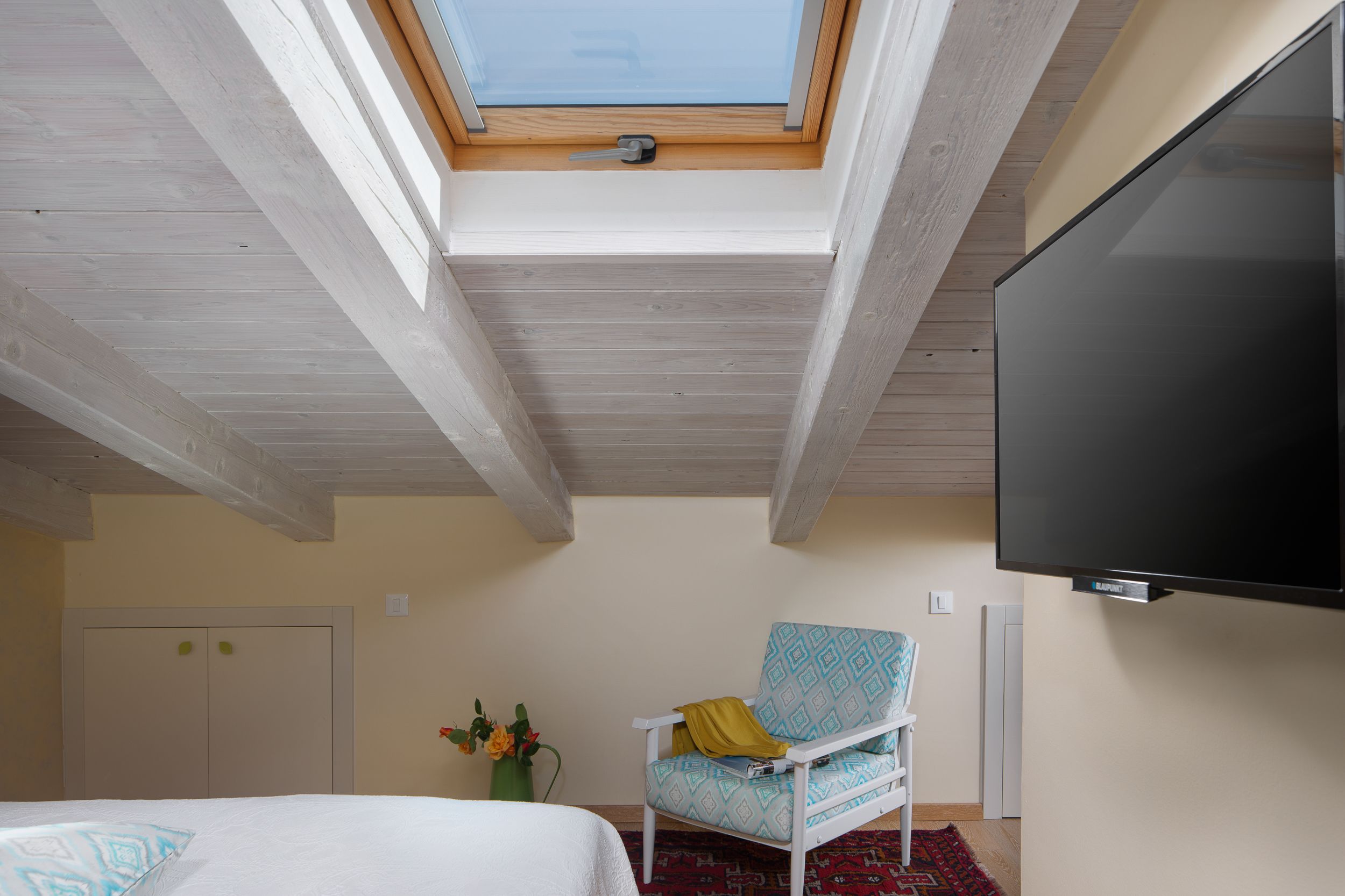 A bedroom with a skylight, a bed, a TV, a chair, and a wardrobe.