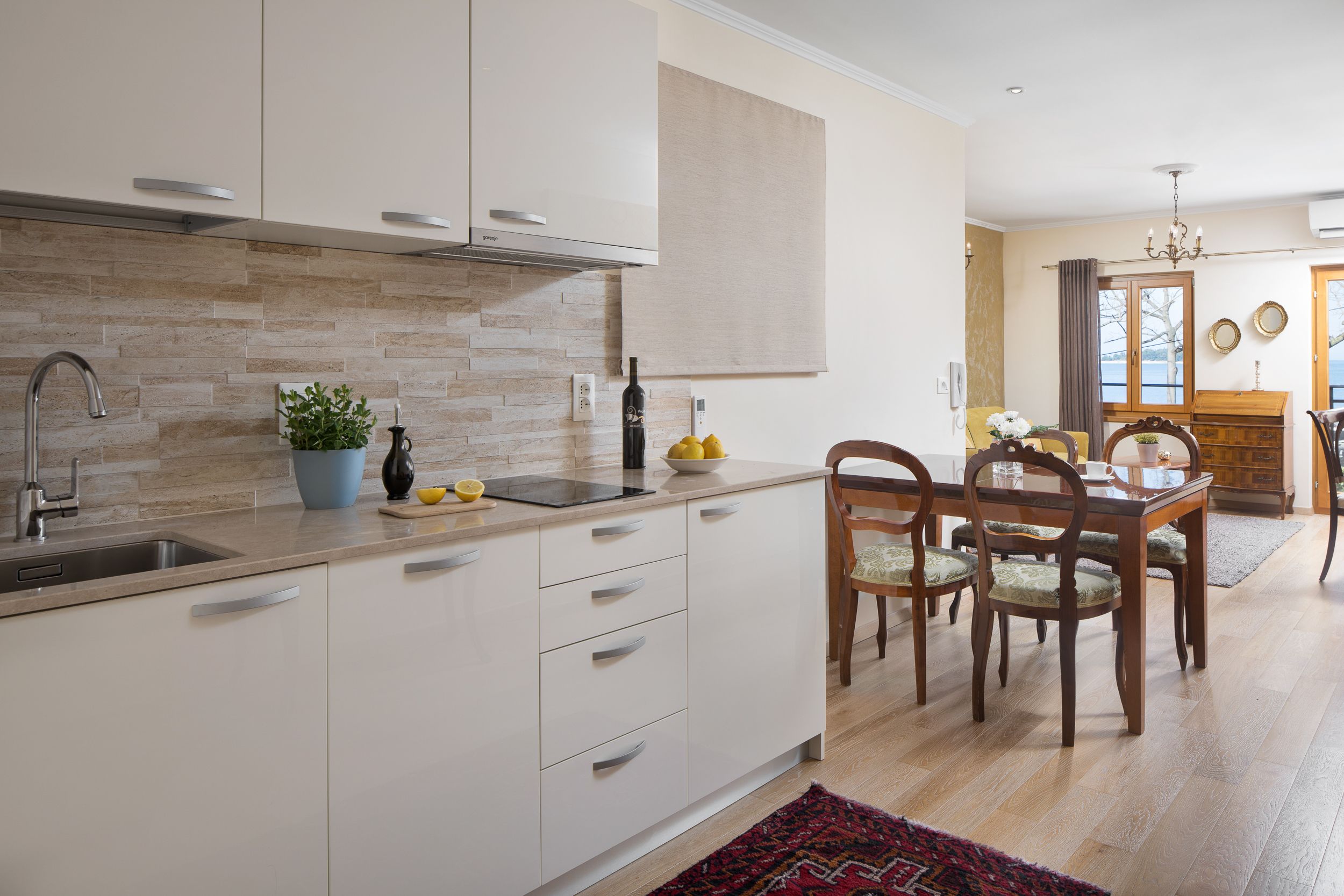 A modern kitchen with white cabinets, a built-in sink, and a dining area with wooden chairs and a table.
