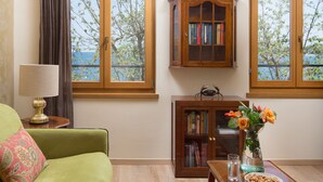 A living room with a green sofa, a wooden cabinet with books, a vase with flowers, and a view of the sea through large windows. - Valdibora Seaview Residence (Rovinj)