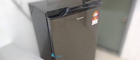 A compact, dark-colored refrigerator with a visible brand label and a sticker on the door.