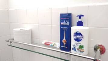 Uma prateleira no banheiro com um rolo de papel higiênico, um shampoo Clear Men Anti-Caspa e um líquido lavante para as mãos antibacterial Follow Me.