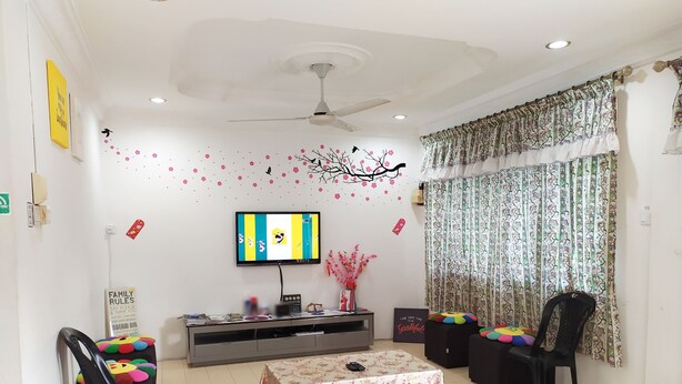 A living room with a flat-screen TV, a ceiling fan, a floral table, and a couch. - H Homestay - Semi D 1000Mbps (1Gbps) Wifi, Astro & Private Parking (Sibu)