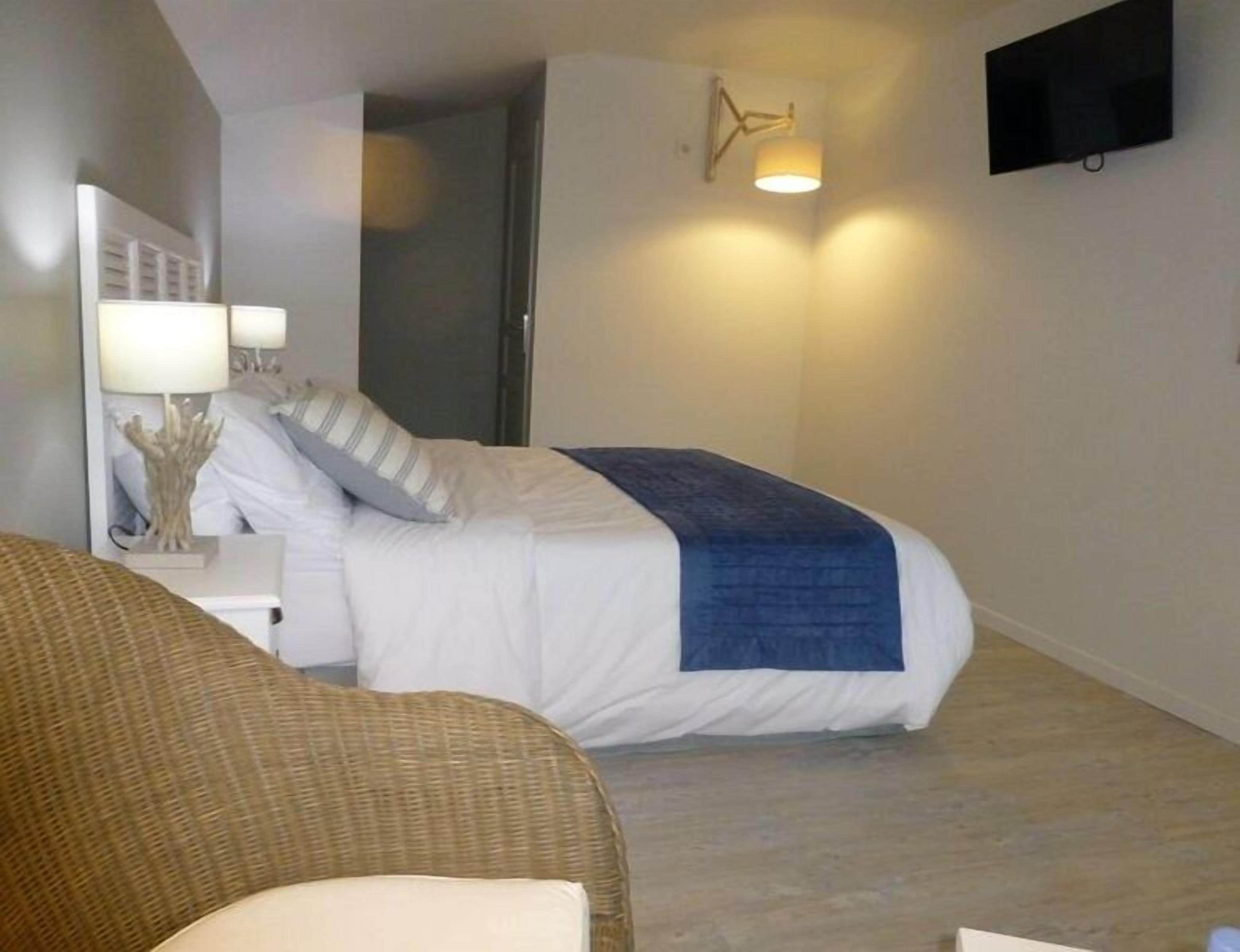 Une chambre d’hôtel comprenant un lit, une table de chevet avec une lampe, un téléviseur fixé au mur et une porte donnant sur une autre pièce.