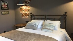 A neatly made bed with a quilted cover, two pillows with text, a metal headboard, a wall-mounted light, and a 'KEEP OUT' sign. - Le Clos Du Miroir (Courset)