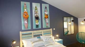 A bedroom with a bed, two bedside tables, a nightstand, a mirror, and three wall-mounted paintings.