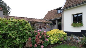 A house with a tiled roof, a garden with various plants, and a window with hanging flowers. - Le Clos Du Miroir (Courset)