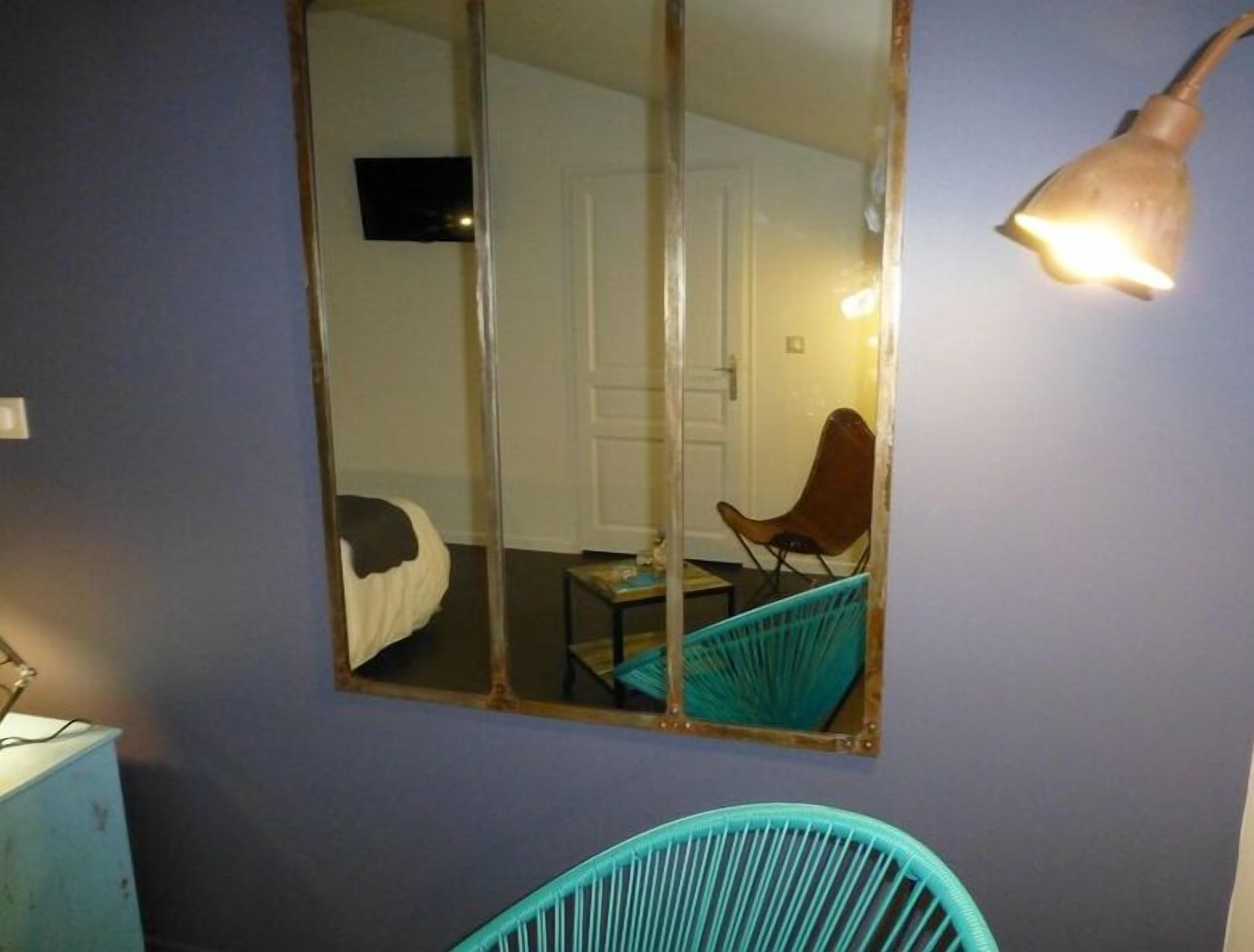 A room with a large mirror reflecting a door and a chair. There is a lamp on the wall.