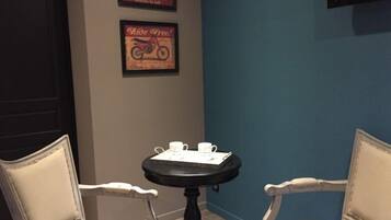 A room with two white upholstered chairs, a small round table with a black base, and two white cups. There are two framed posters on the wall, one with a motorcycle and the other with the text "Ride Free!" The room has a blue accent wall and a black door.