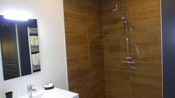 Une salle de bain avec un lavabo blanc, un miroir et une douche équipée d’un pommeau de douche à main.