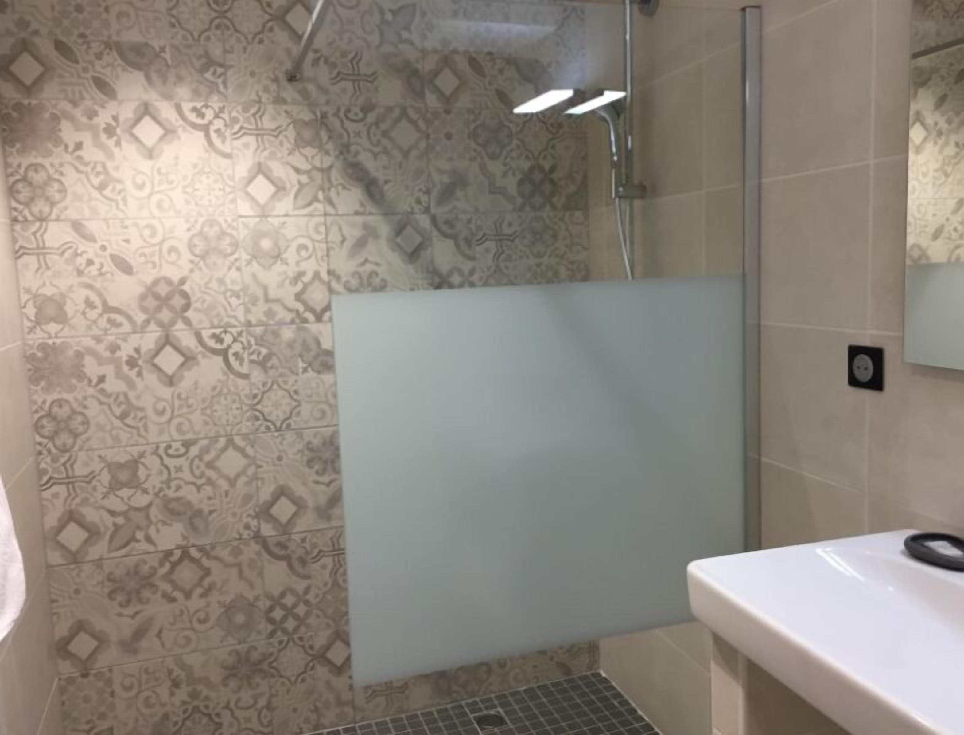 Une salle de bain avec des carreaux décorés, un espace douche et un lavabo blanc.