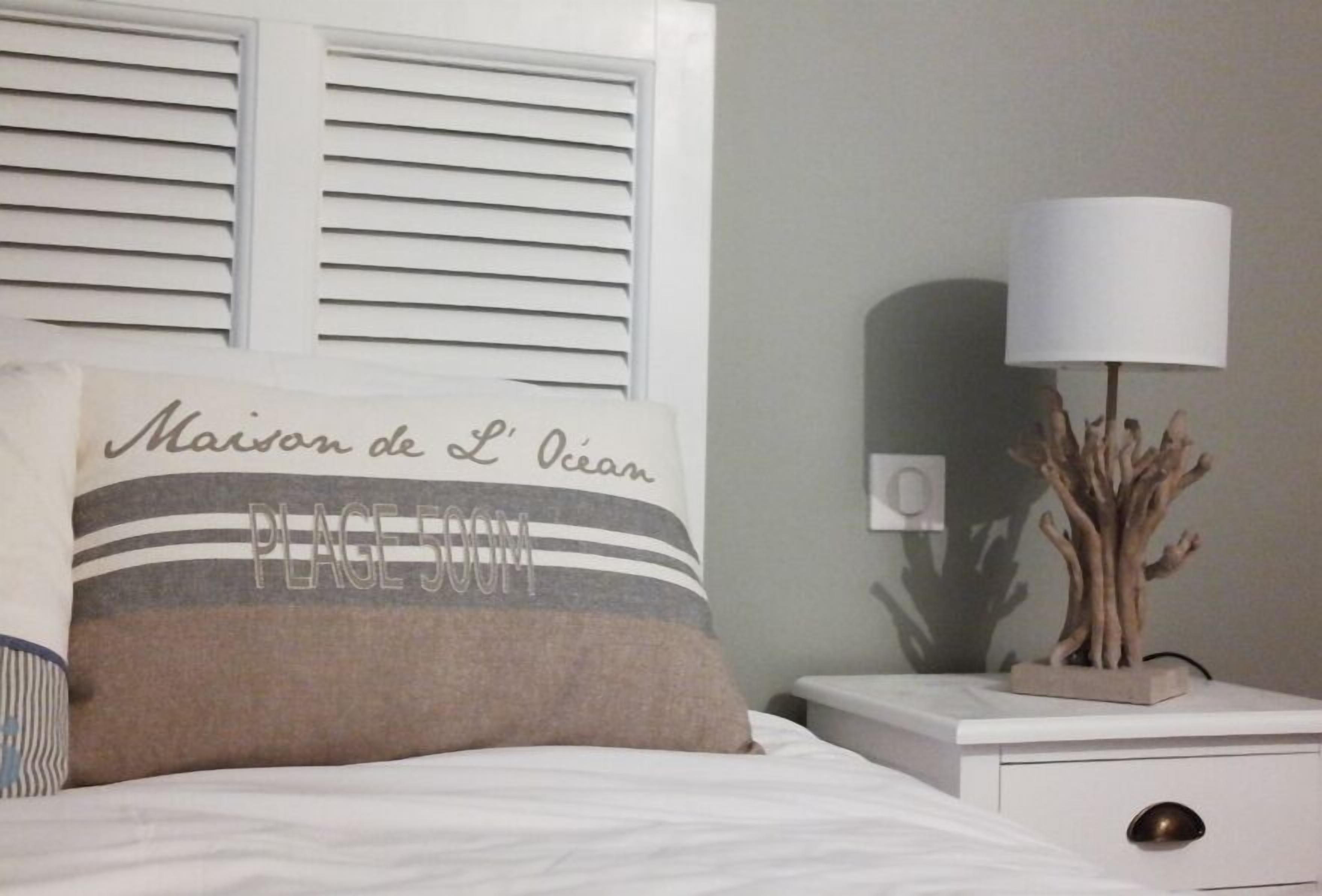 A neatly made bed with a pillow that reads "Maison de L'Ocean" and "PLEASE DOWN."