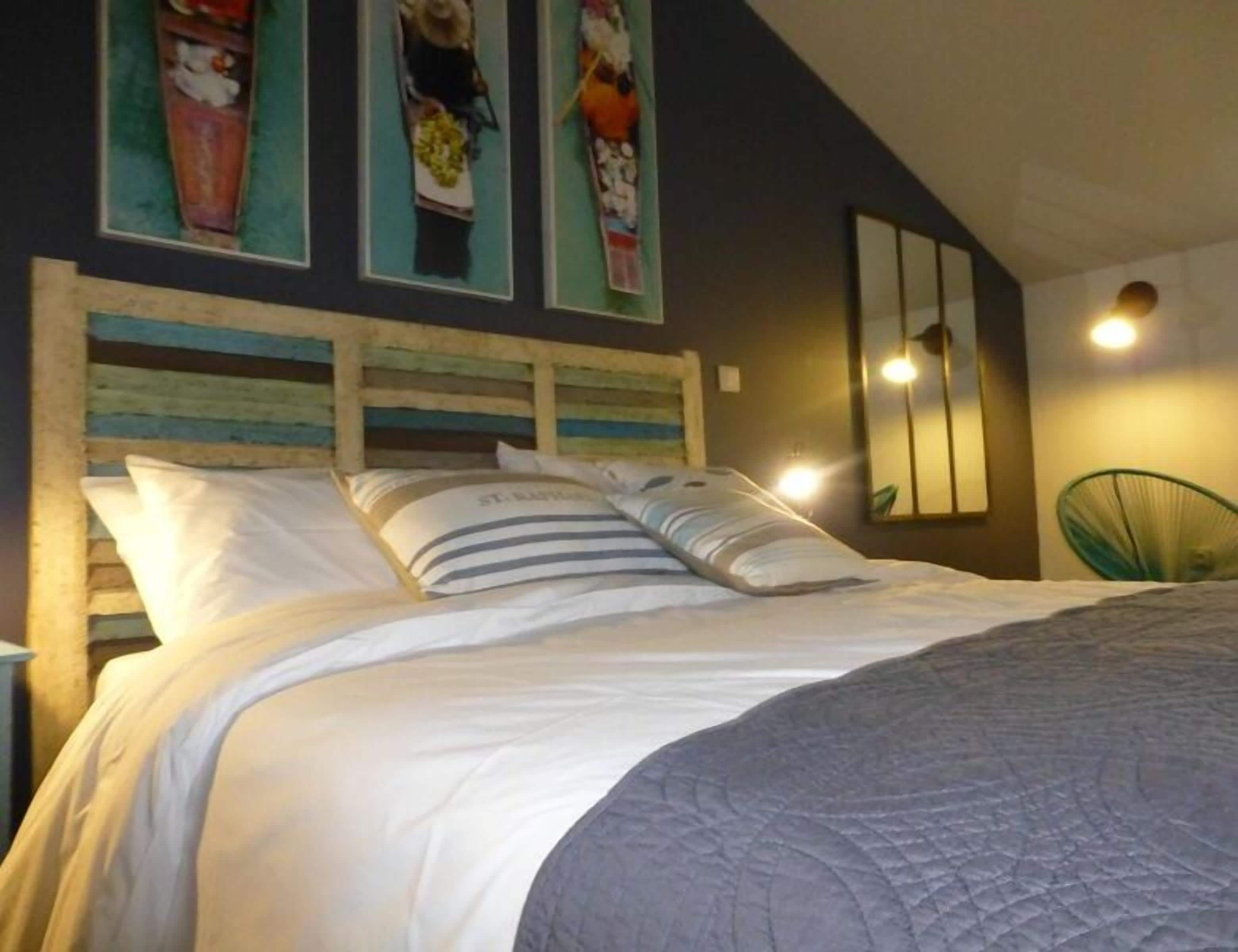 Una cama con cabecera de madera, ropa de cama blanca y almohadas a rayas. Se observan obras de arte colgadas en la pared sobre la cama.