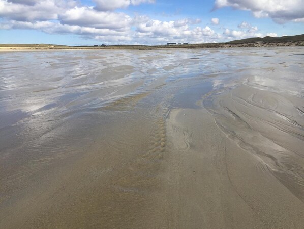 A wide, flat beach with gentle waves and a clear sky.
