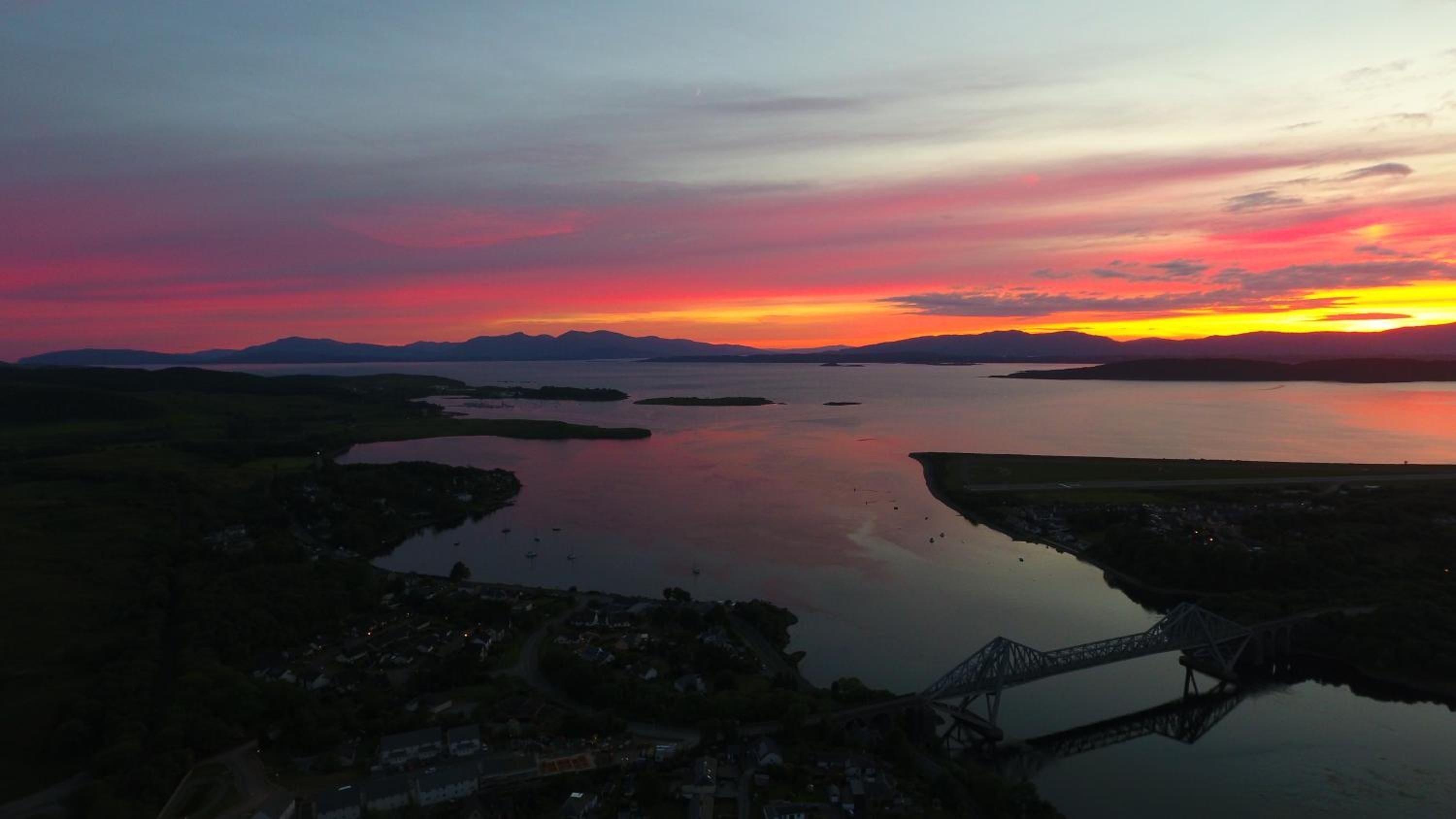 A sunset over a calm lake with a bridge and a small town in the foreground.