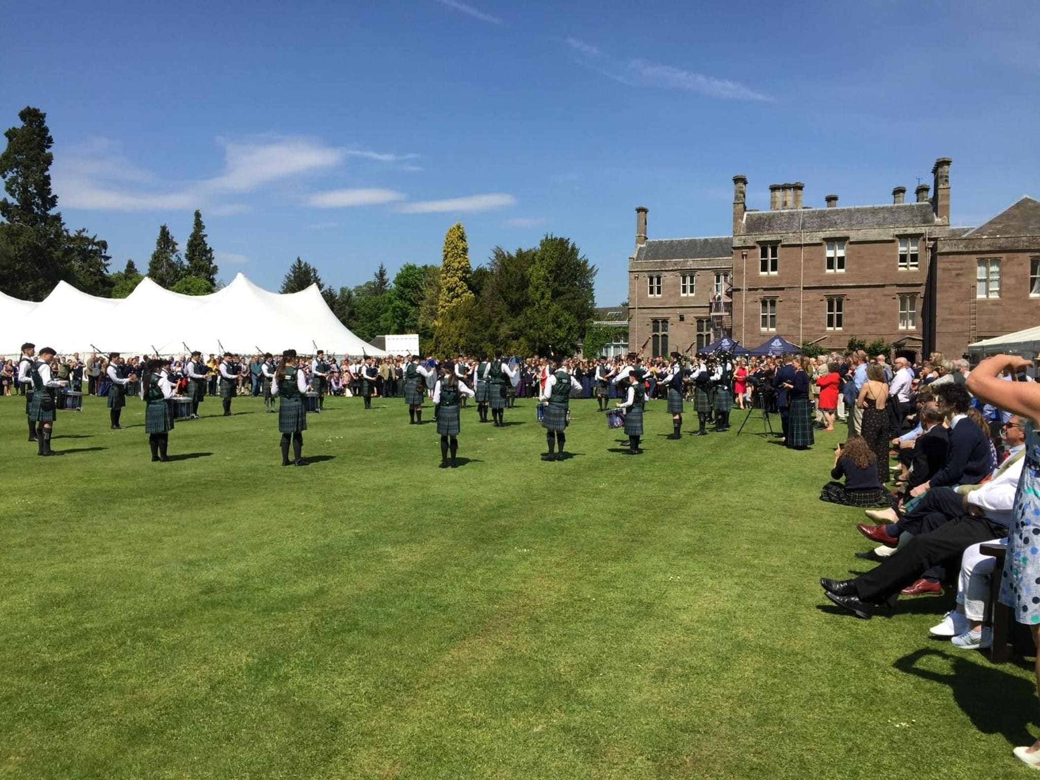 A group of people in kilts performing in an open field with a building in the background.