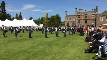 A group of people in kilts performing in an open field with a building in the background.