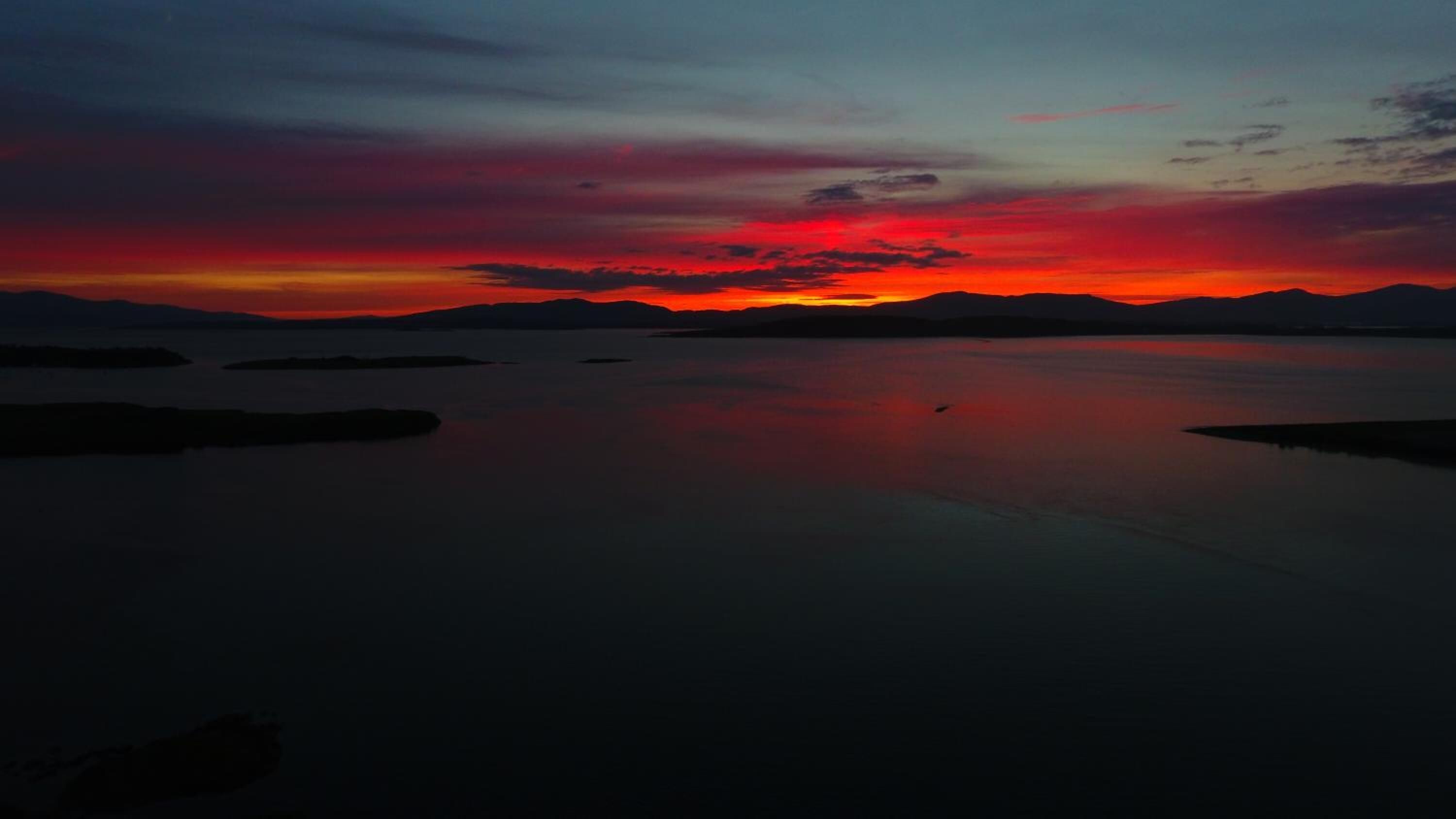 Ein ruhiger See bei Sonnenuntergang, im Hintergrund Berge.