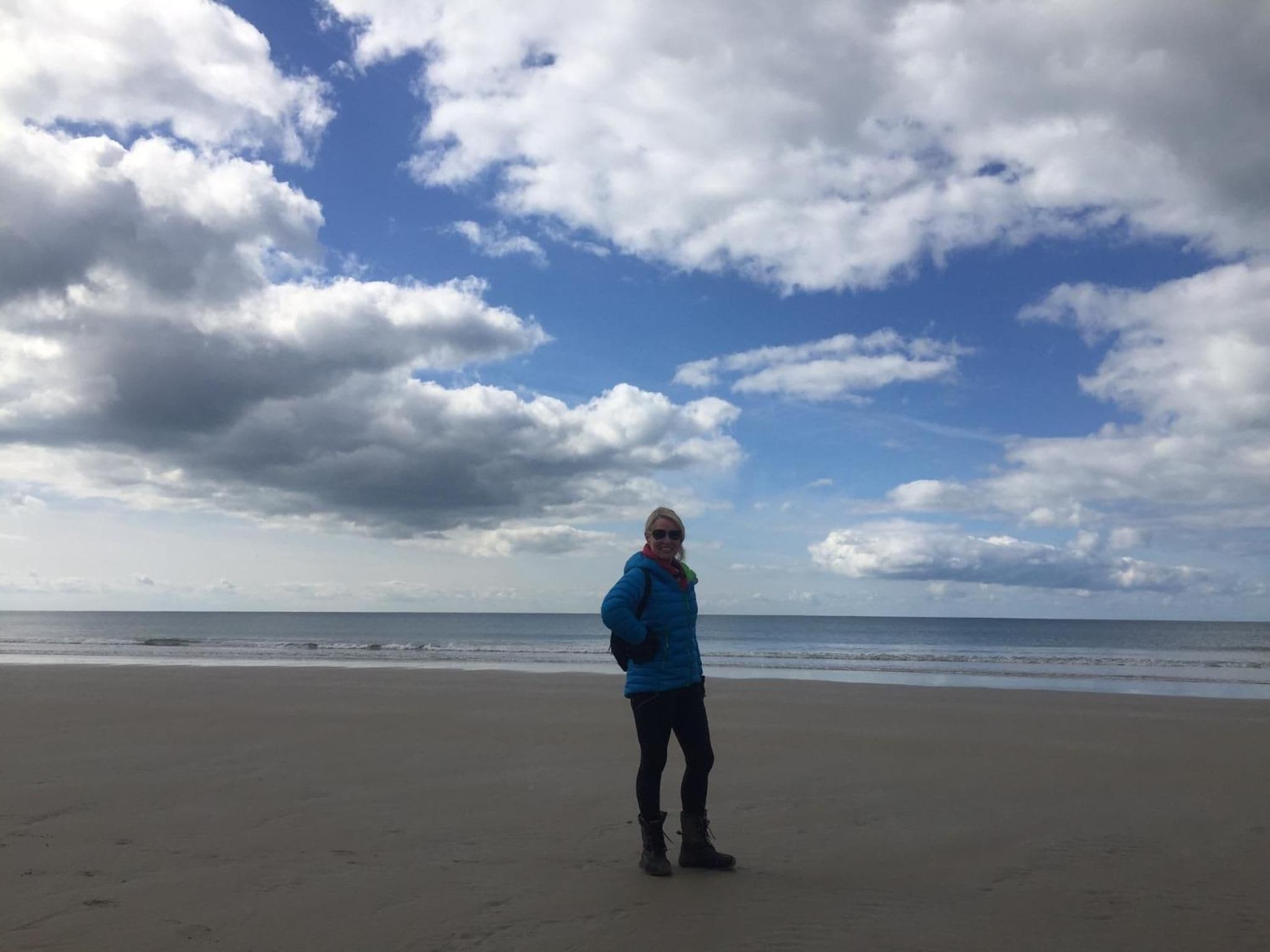 A person standing on a sandy beach with a cloudy sky.