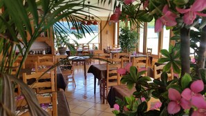 Un restaurant avec des meubles en bois, de grandes fenêtres et des plantes en pot.