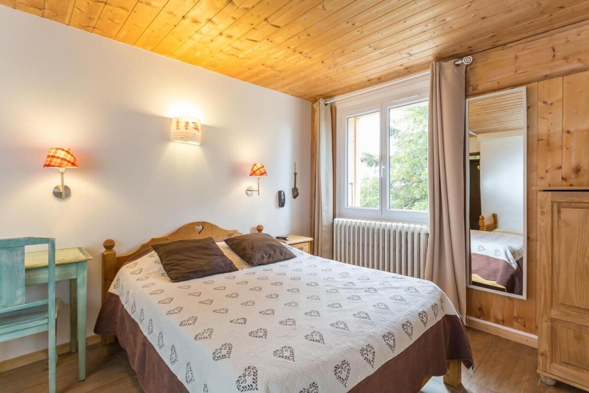 A wooden-paneled bedroom with a bed, two wall-mounted lamps, a window with curtains, and a radiator.