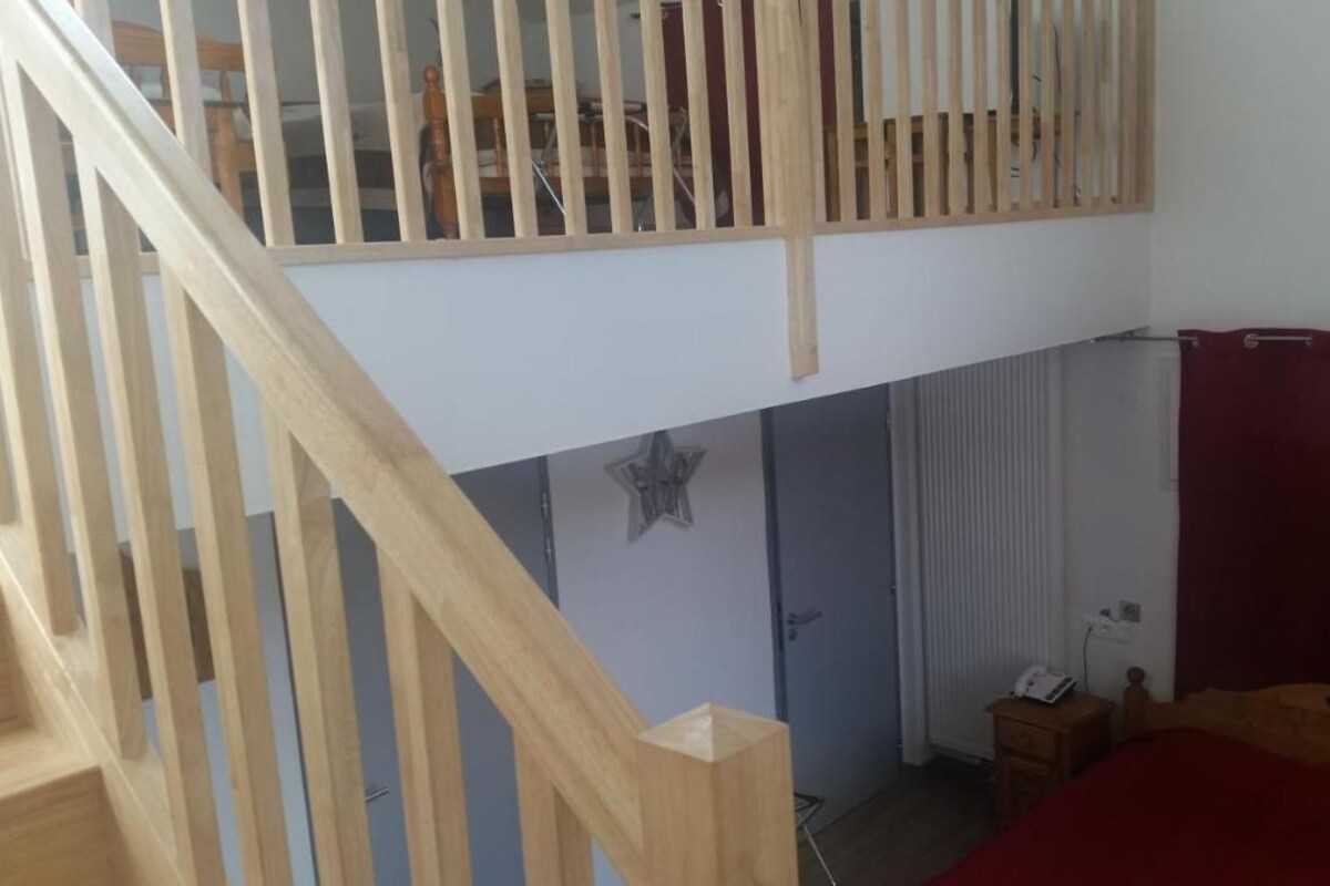 A bedroom with a wooden staircase, a bed with a red blanket, a bedside table, and a radiator.