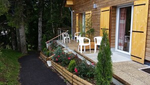 Un bâtiment en bois doté d’un espace extérieur abrité avec des sièges, d’un chemin de gravier et d’un petit jardin agrémenté de fleurs et d’arbustes.