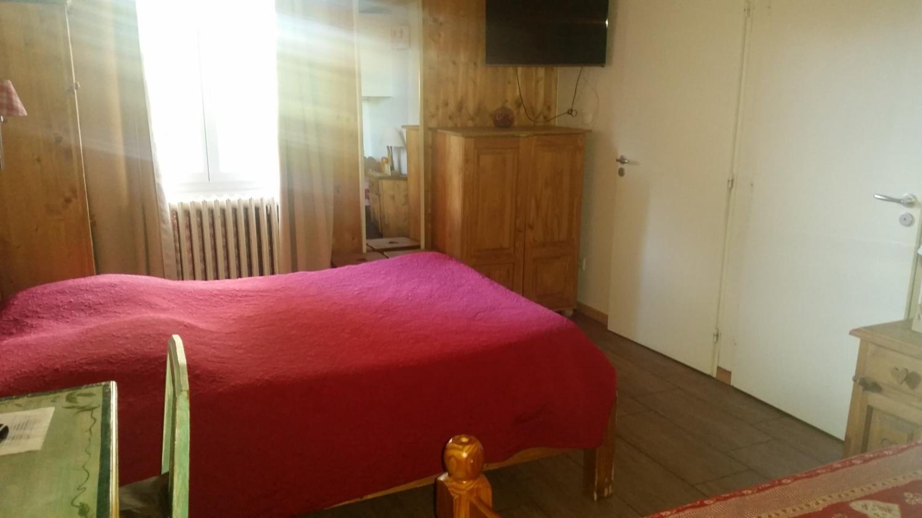 A room with a bed, wooden wardrobe, and a television mounted on the wall.
