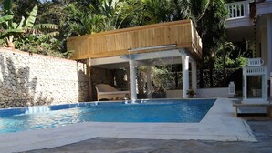 A swimming pool with a stone wall and a wooden deck. - Casa Estrella Mirabal (Cabarete)