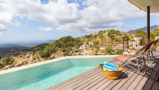 Una terraza de madera con piscina, sillas de descanso y un cesto con toallas.