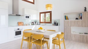 Una cocina moderna con armarios blancos, una mesa de comedor de madera con sillas amarillas, un horno empotrado y una ventana con vistas a árboles.