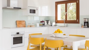 Una cocina moderna con muebles blancos, microondas integrado, horno y una mesa de comedor con sillas amarillas.
